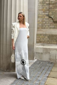 Robe longue blanche ornée d'un grand imprimé floral noir et blanc, associée à un blazer structuré crème et un sac tissé crème.