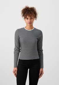 Schwarz-weiß gestreiftes Langarmshirt mit rundem Halsausschnitt, gerippter Textur und figurbetontem Design, kombiniert mit schwarzen Hosen.