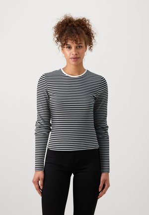 Svart og hvitstripet langermet skjorte med rund hals, ribbelt tekstur og tettsittende design, kombinert med svarte bukser.