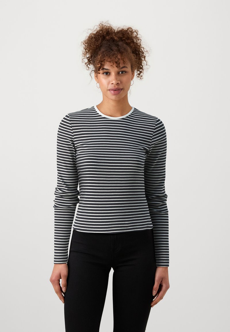 Schwarz-weiß gestreiftes Langarmshirt mit rundem Halsausschnitt, gerippter Textur und figurbetontem Design, kombiniert mit schwarzen Hosen.