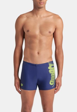 Costumi da bagno blu navy con un design aderente, caratterizzati da un vivace logo del marchio giallo sul lato e una texture liscia e elastica.
