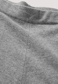 Nahaufnahme eines grauen Stoffs mit weicher Textur, leicht meliertem Muster und einem nahtlosen, abgerundeten Taillenbund mit gesteppter Mittelnaht.