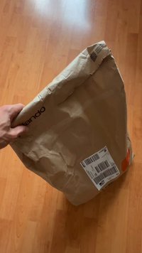 Rjav papirni paket, ki ga držijo, z logotipom in poštnim oznako z črtno kodo, guban tekstura in odprto vrh.