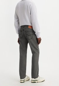 Jeans de mezclilla gris con diseño clásico de cinco bolsillos, que presentan costuras en contraste, una etiqueta de cuero en la cinturilla y un aspecto envejecido. Se combinan con un suéter gris y zapatillas blancas.