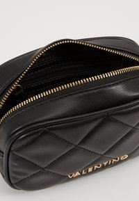 Borsa in pelle nera con design a trapuntatura, cerniera dorata e marchiata "Valentino" in lettere dorate. L'interno presenta diverse tasche.