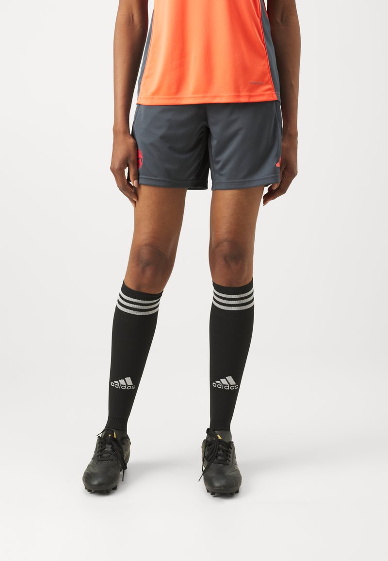Botas de fútbol negras, pantalones cortos grises con detalles rojos, camiseta naranja. Medias negras hasta la rodilla con rayas blancas y logo.