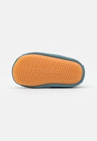 Blaues Stoffoberteil mit orangefarbener Gummisohle, die ein wellenförmiges Muster und ein geprägtes Logo aufweist. Entworfen mit glatten Kanten und runder Form.