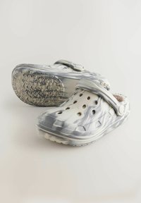 Sabots marbrés blancs et gris avec des trous de ventilation, une sangle, une semelle en caoutchouc texturée et un bout arrondi pour le confort et la stabilité.
