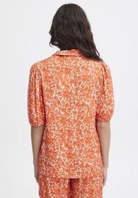 Orange floral print blouse with a relaxed fit, puffed sleeves, and a button-up collar. Fabric appears lightweight and textured.