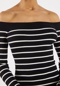 Top nero a spalle scoperte con texture a coste verticali, caratterizzato da strisce orizzontali bianche. Design aderente.