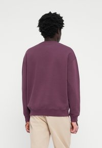Purple sweatshirt with a crew neckline, drop shoulder design, ribbed cuffs, and hem, paired with beige pants. Simple and casual style.