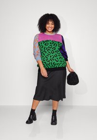 Knit sweater with leopard pattern in green, purple, and gray, paired with a black satin midi skirt; holding a black textured handbag.