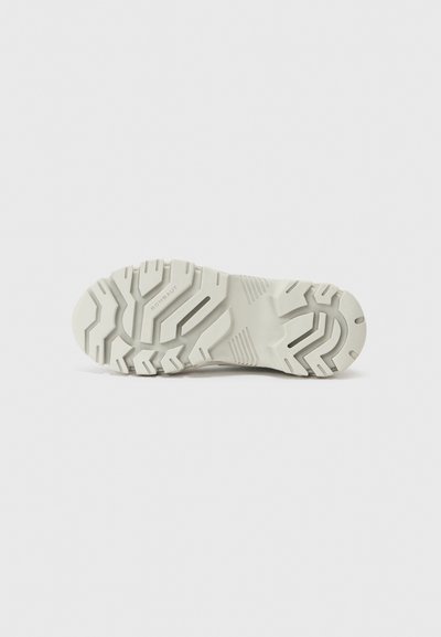 Semelle de basket blanche en caoutchouc texturé, avec de profonds sillons pour une meilleure adhérence et un branding subtil sur le côté. Design minimaliste.