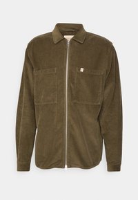 Olivově zelená manšestrová bunda se zipem vpředu, špičatým límcem a dvěma náprsními kapsami. Má žebrovanou texturu a malou značkovou cedulku na kapse.