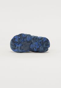 Suela de zapato de goma negra y azul con patrones texturizados y relieves para un mejor agarre. El diseño incluye un logo en el costado.