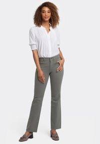 Blusa blanca ligera con pliegues, combinada con pantalones rectos verde olivo. El modelo lleva mocasines de ante grises con detalles de lazos.