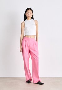 Top corto sin mangas blanco, pantalones de pierna ancha rosa con pliegues frontales y mocasines negros. Textura suave y diseño ajustado.
