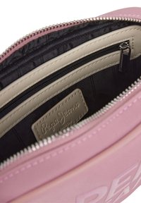 Roze synthetische tas binnenkant met zwarte voering, één ritsvak en een beige label met "Pepe Jeans London" gegraveerd.