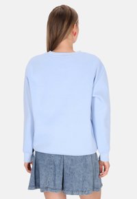 Sudadera azul claro con mangas largas, cuello redondo y puños acanalados, combinada con una falda plisada de mezclilla. Vista trasera que muestra un diseño sencillo.