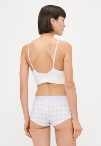 Fehér bordázott bralette állítható pántokkal, világoslila rövidnadrággal párosítva, amely gyémánt mintázattal és puha derékrésszel rendelkezik.