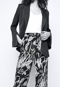 Svart kavaj med utsvängda ärmar över en vit topp, tillsammans med hög midja svarta och vita byxor med bladmönster.