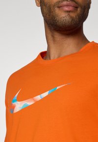 Oranje katoenen T-shirt met ronde hals en een textuur Nike swoosh logo met blauwe en witte accenten.