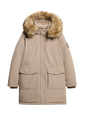 Parka beige avec une capuche en fausse fourrure, deux grandes poches avant, fermeture à boutons-pression et un logo sur la manche gauche. Tissu doux et texturé.
