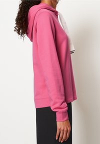 Roze hoodie met witte trekkoorden, met lange mouwen en ribgebreide manchetten, zijaanzicht weergegeven. Zachte stof en een relaxte pasvorm.