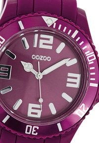 Montre en silicone violet avec un cadran rond, des marqueurs d'heure blancs et une lunette en acier inoxydable. Résistante à l'eau avec des marques numérotées à des intervalles.