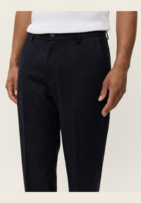 Tailored dark navy trousers made from a textured fabric, featuring a traditional waistband with a button, side pockets, and a slim fit design.