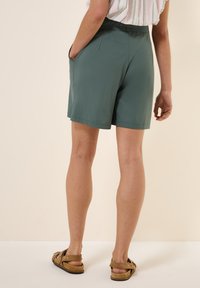 Pantaloni corti verdi in tessuto morbido con cintura elastica e tasche laterali. Il design presenta un taglio dritto e una lunghezza fino a metà coscia.