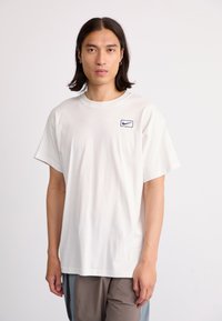 Hvid bomulds t-shirt med rund hals og korte ærmer, prydet med et lille blåt Nike-logo på venstre bryst. Glat tekstur, afslappet pasform.