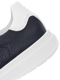 Lähikuva mustasta teksturoidusta nahkaisen lenkkarin kantapäästä, jossa on valkoinen nahkakaulus ja paksu valkoinen kumipohja.