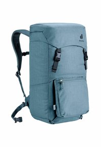 Mochila de tejido azul claro con un diseño rectangular. Presenta correas ajustables, cierre con solapa superior, bolsillo frontal con cremallera y detalle del logo.