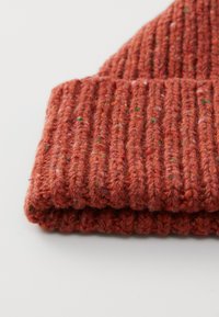 Bonnet en tricot côtelé plié de couleur rouille orangé mouchetée, mettant en valeur des fibres de laine texturées, sur une surface claire.