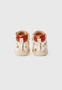 White ankle boots featuring tan polka dots, a shiny red heel, and a gold accent. Soft inner lining and a flat sole design.