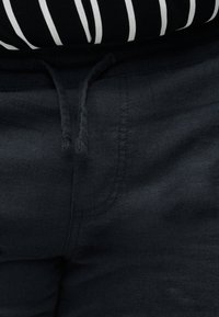 Κοντινό πλάνο σκούρων μπλε παντελονιών με κορδόνι στη μέση και μέρος ενός μαύρου και άσπρου ριγέ τοπ να φαίνεται από πάνω.