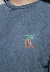 Blue cotton T-shirt featuring a textured finish and a small chili pepper graphic in red and green on the chest.