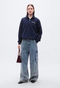 Μπλε σκούρο φούτερ με φερμουάρ μέχρι τη μέση και το λογότυπο "TOMMY JEANS", συνδυασμένο με μπλε τζιν παντελόνι cargo με φαρδιά μπατζάκια, τσέπες με πατς και υφή ύφασματος.