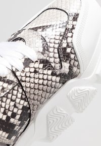 Sneaker z czarno-białym wzorem węża, górna część z teksturowanej skóry, biała gumowa podeszwa i białe sznurówki.