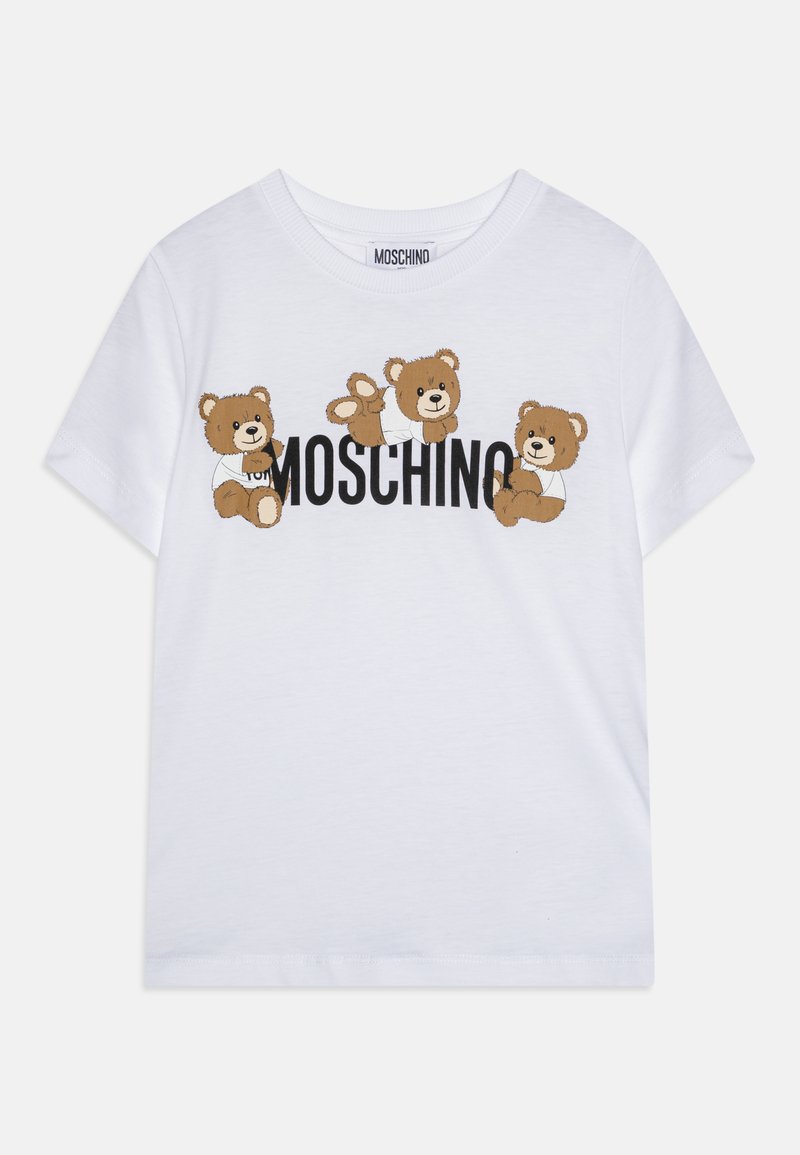 Balta kokvilnas t-kreklā ir trīs brūnu lācīšu grafikas un vārds "MOSCHINO" uzrakstīts treknajā melnajā tekstā krūšu rajonā. Īsas piedurknes, apaļa apkakle.