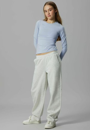 Lichtblauw aansluitend shirt met lange mouwen, gecombineerd met lichtgrijze joggingbroek met steekzakken aan de zijkant, afgewerkt met witte sneakers. Gladde stoftextuur.