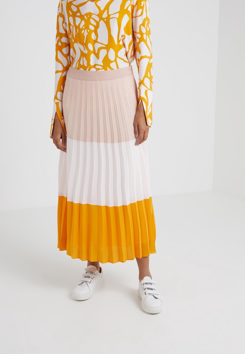 Jupe plissée en dégradé orange, blanc et rose ; associée à une chemise à manches longues avec un motif abstrait jaune. Baskets blanches.