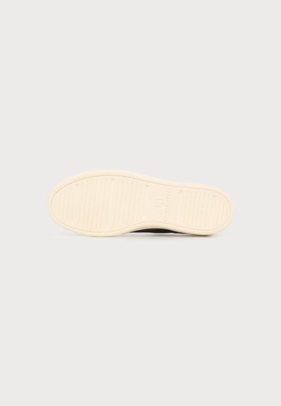 Semelle d'une chaussure beige à semelle en caoutchouc avec des rainures horizontales et un motif de logo rectangulaire au centre sur un fond uni.