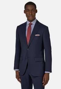 Navyblauw pak met een getailleerde pasvorm, voorzien van een notch-revers, twee voorkeursvakken en bijpassende broek. Gestreept overhemden met een rode das als accent.