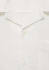Camicia bianca a maniche corte con un motivo a strisce testurizzato. Dotata di un colletto a scollo, un singolo taschino anteriore e una chiusura a bottoni.