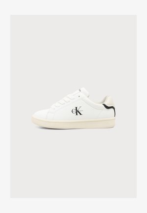 Baskets basses blanches Calvin Klein avec semelle beige, détail talon noir, fermeture à lacets et logo "CK Calvin Klein" sur le côté.