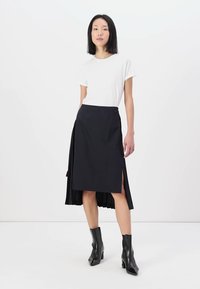 Fustă neagră până la genunchi, cu spate plisat și deschidere laterală, asortată cu un tricou alb cu mânecă scurtă și botine negre. Textură netedă.