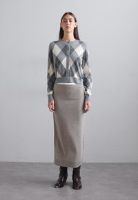 Grå cardigan med argyle-mønster i kremfarge og mørkegrå diamanter, knapper foran, kombinert med et beige strikket skjørt og brune skinnankelboots.