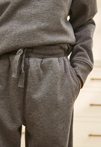 Sweatshirt en coton gris et pantalon avec taille élastique. Les pantalons disposent d'un cordon de serrage et de poches latérales. Texture douce et coupe décontractée.